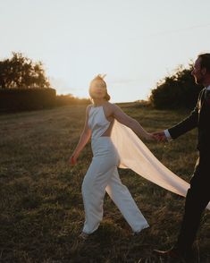 a bride and groom hold hands as the sun sets behind them in an open field