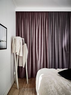 a white bed sitting next to a window covered in purple drapes on top of a wooden floor