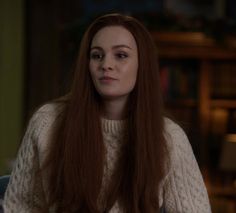 a woman with long red hair sitting in a chair looking at the camera while wearing a sweater