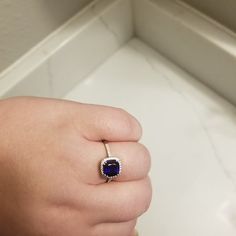 a person's hand holding a ring with a blue stone on it and a white background