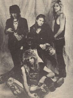 an old black and white photo of four young men with long hair sitting on the ground