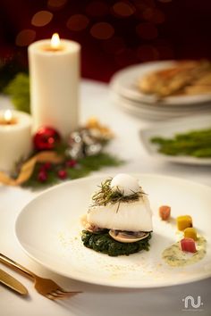 a white plate topped with food on top of a table next to candles and plates