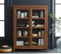 a wooden cabinet with glass doors next to a vase and other items on the floor