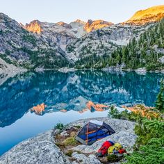 a tent is set up on top of a rock near a lake with mountains in the background