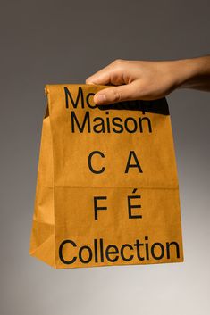 a person's hand holding a brown paper bag with the words mcason cafe collection on it