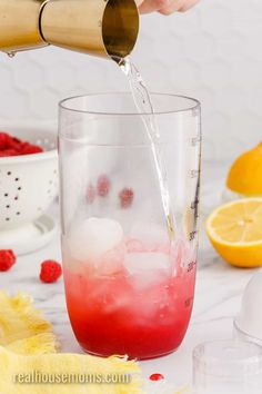 someone pouring water into a glass with raspberries and lemons in the background