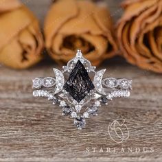 a black and white diamond ring sitting on top of a wooden table next to roses