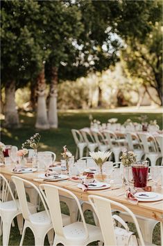 a long table is set with white chairs and place settings for an outdoor wedding reception