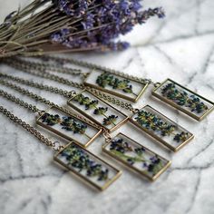 six necklaces with flowers in them sitting on a marble table next to some dried lavender