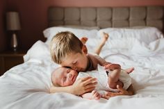 a young boy laying on top of a bed holding a baby