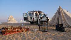 an suv parked in the sand next to a tent and some bags on the ground