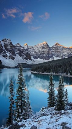 the mountains are covered in snow and there is a blue lake surrounded by pine trees