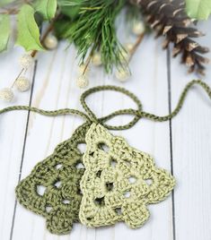 three crocheted ornaments are sitting on a white table next to pine cones and greenery