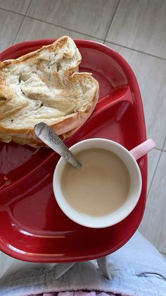 a red plate topped with a piece of bread next to a cup of hot chocolate