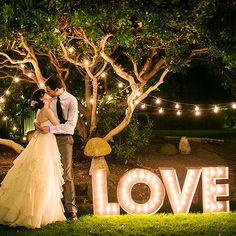 a couple standing next to each other in front of a tree with lights on it