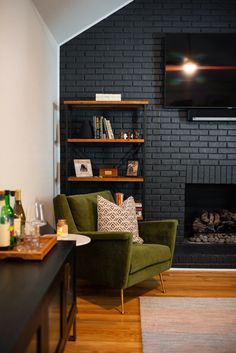 a living room with black brick walls and green chairs in front of the fire place