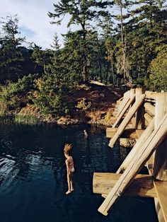 a woman is standing in the water next to some wooden structures and logs that are floating on top of the water