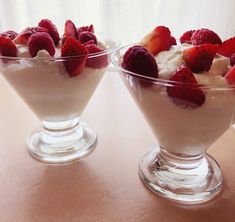 two dessert dishes with strawberries and whipped cream in them on a table top,