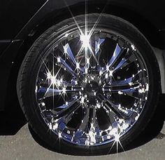 the front wheel of a black car with chrome spokes and bright lights on it