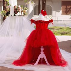 a red dress is on display in front of a white wedding veil and flower arrangement