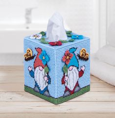 a blue tissue box with gnomes on it sitting on a wooden table next to a toilet paper roll