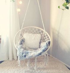 a white hanging chair in a room with a potted plant next to it and a pillow on the floor