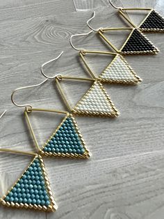 four pairs of triangle earrings with beaded ends on a wooden surface, one is blue and the other is white