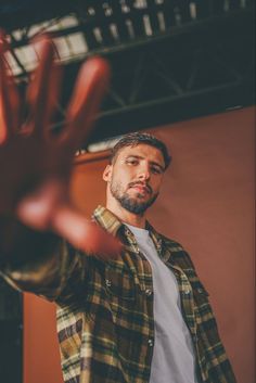 a man holding his hand up in the air while wearing a plaid shirt and white t - shirt