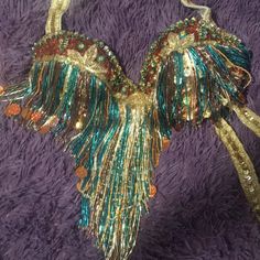 an angel wings ornament hanging on a purple blanket with gold and green sequins