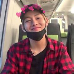 a young boy wearing a black mask with pink hearts on it's head and sitting in a bus