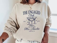 Celebrate your special moment with our cozy and stylish "The Engaged Club" sweatshirt! Perfect for newly engaged couples, this sweatshirt features a chic design that proudly announces your new status in the most comfortable way possible. Crafted from a soft, high-quality cotton blend, it offers a relaxed fit that's perfect for lounging at home or running errands. The elegant script is printed with eco-friendly ink, ensuring it remains vibrant and lovely wash after wash. Available in a variety of Fiance Sweatshirt, Engagement Gifts For Bride, Mrs Sweatshirt, Bride Sweatshirt, New Status, Gifts For Bride, Newly Engaged Couple, Club Sweatshirts, Gift For Bride