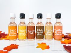 four bottles with labels on them sitting next to autumn leaves