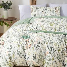 a bed with white and green comforter next to a potted plant on a table