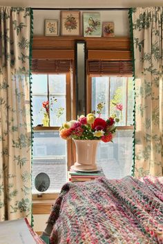 a vase with flowers sitting on top of a bed in front of a large window