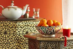 oranges are in a bowl on a table next to a teapot and cups