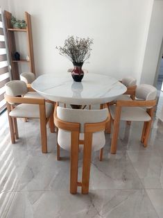 a white table with six chairs and a vase on the top is in an empty room