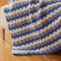 a crocheted blanket sitting on top of a white chair next to a wooden floor