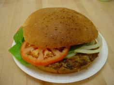 a sandwich with lettuce, tomato and onion on a white plate sitting on a wooden table