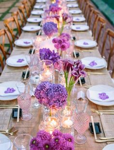 a long table is set with purple flowers and candles for an elegant dinner or party