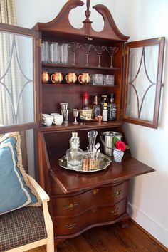 an old fashioned wooden cabinet with wine glasses and other items on it's shelf