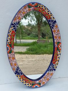 a colorful mirror sitting on top of a white table next to a tree and grass