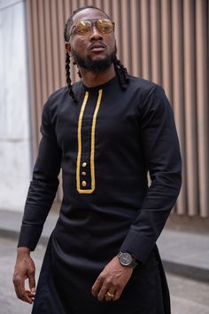 Elevate your style with our Black African Tunic for Men, meticulously designed with contemporary flair and traditional influence. Adorned with striking gold trim and golden buttons, this tunic seamlessly merges modern fashion with authentic African charm. Key Features: - Versatile Elegance: Our African Tunic is a perfect blend of tradition and modernity, suitable for special occasions and cultural events or for making a stylish statement in everyday wear. - Captivating Details: The classic black hue is complemented by luxurious gold trim and tasteful gold buttons, adding an opulent touch to your ensemble, ensuring you stand out with elegance. - Comfortable Fit: Designed for comfort and style, our Tunic for Men provides unrestricted movement while maintaining an air of grace, ensuring you f Tunic For Men, African Wear Designs, Black And Gold Outfit, Outfit Traditional, Latest African Wear For Men, African Wear For Men, Dashiki For Men, Nigerian Outfits, African Tops