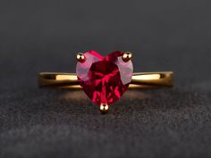 a red heart shaped ring with two small hearts on the front and side, sitting on a black surface