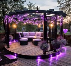 an outdoor gazebo with purple lights on the sides and furniture in the middle, surrounded by greenery