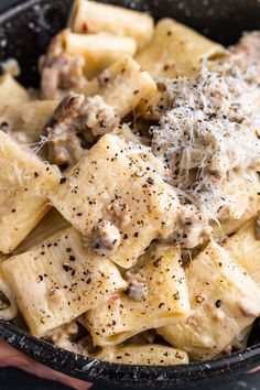 a black bowl filled with pasta and meat covered in cheese sprinkled on top