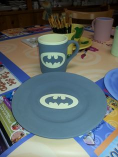 a batman themed plate and cup on a table with other plates, cups and utensils