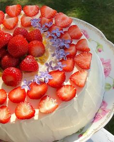 a white cake with strawberries and flowers on it sitting on top of a table