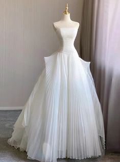 a white wedding dress is displayed on a mannequin in front of a curtain