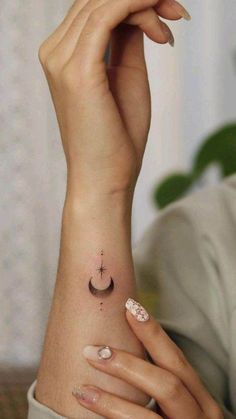 a woman's hand with a small tattoo on her left arm and the moon above it