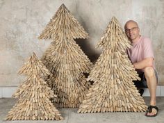 a man sitting on the ground next to two wooden christmas trees made out of sticks